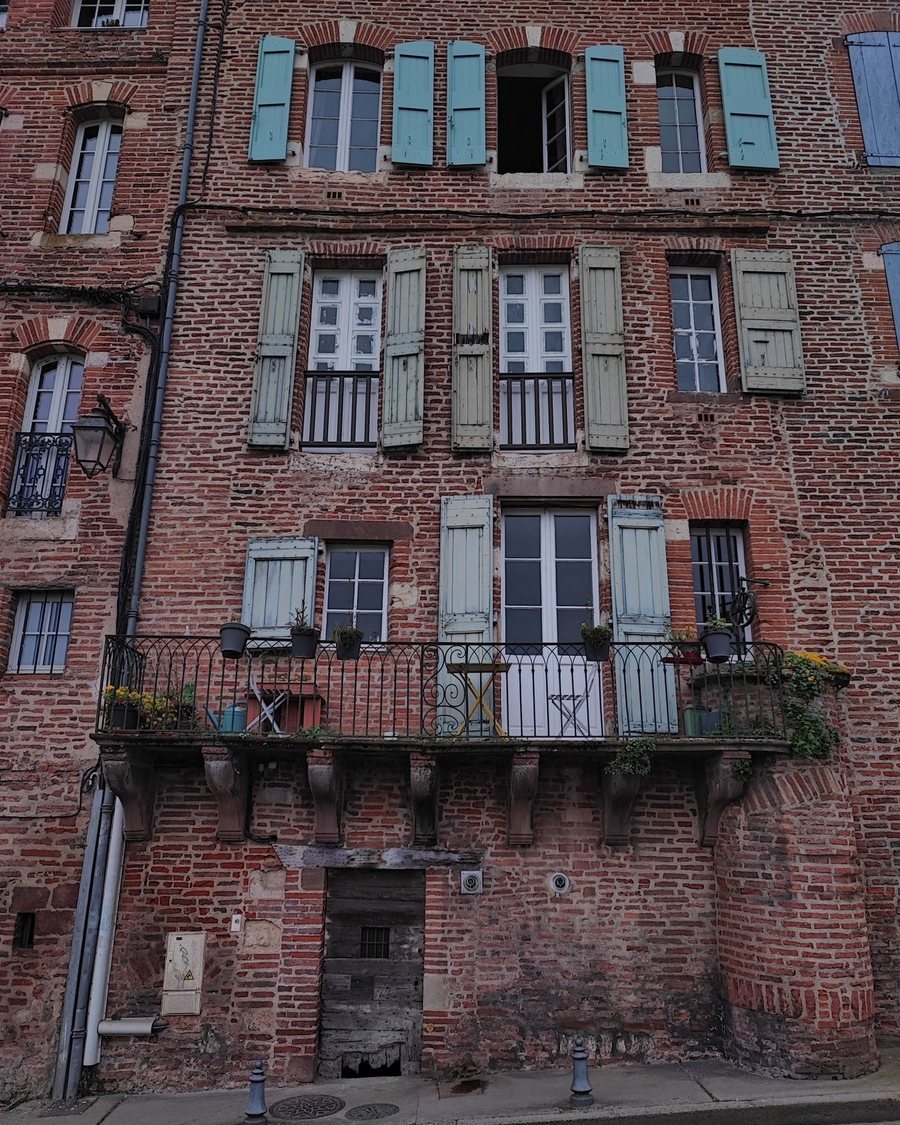 Immeuble ancien en brique à Albi, volets bois défraîchis et balcon en fer forgé